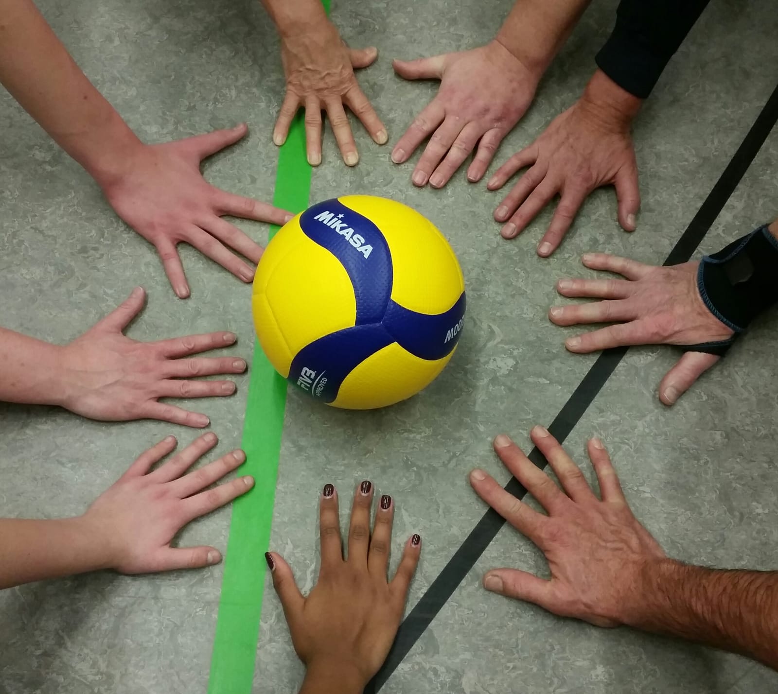 Volleyball in der Mitte und Hände ringsum